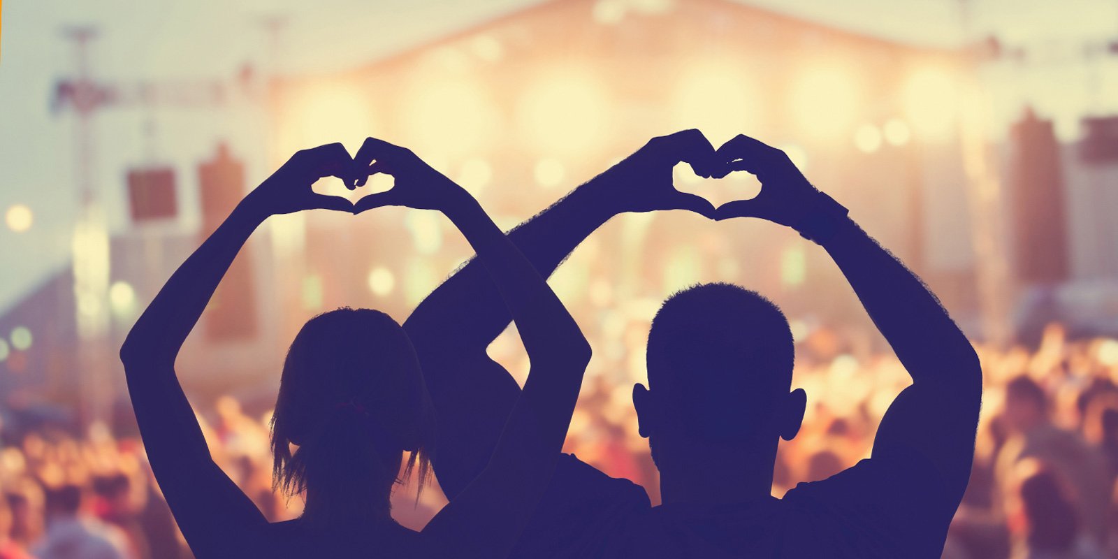 Silhouette of two people at a music festival making heart shapes with their hands